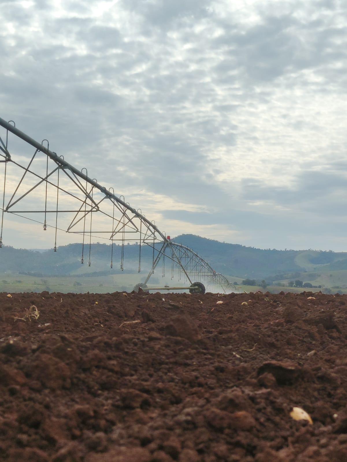 Vista de um pivô de irrigação em campo aberto, com serras ao fundo.
